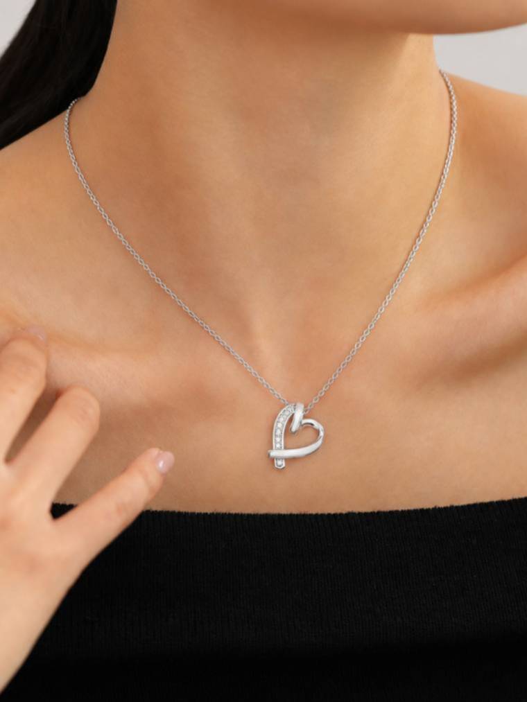 Silver crystal heart pendant necklace worn on a woman's collarbone over a black top, showing pendant size and chain length