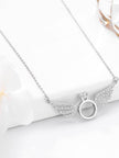 Angel wings ring necklace laid flat on white surface with flower petals beside it