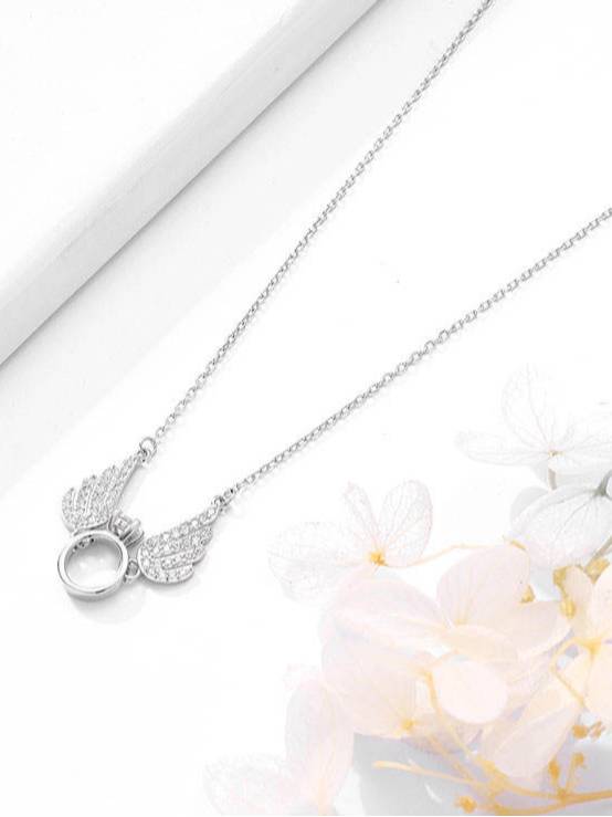 Close-up of angel wings pendant necklace resting on white surface with flowers