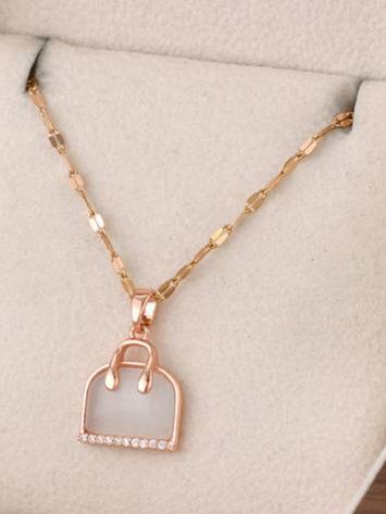Rose gold handbag pendant necklace displayed on a beige jewellery tray