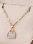 Rose gold handbag pendant necklace displayed on a beige jewellery tray