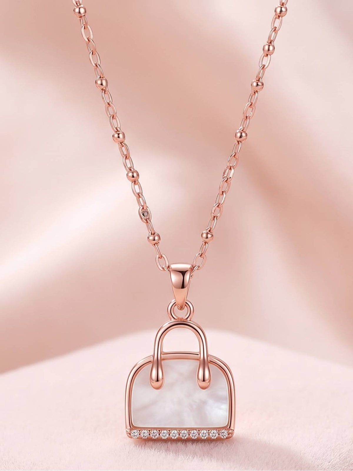 Full view of rose gold satellite chain necklace with handbag pendant on pink background