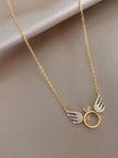 Gold-plated angel wings ring charm necklace laid flat on a beige fabric background