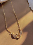 Angel wings ring pendant necklace on a warm tan fabric with soft shadow detail