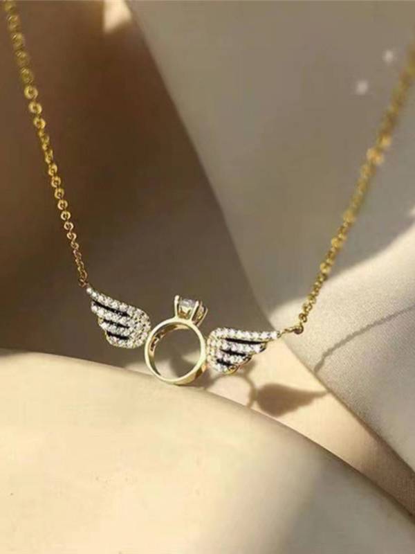 Close-up of gold angel wings ring necklace resting on a cream surface in warm light