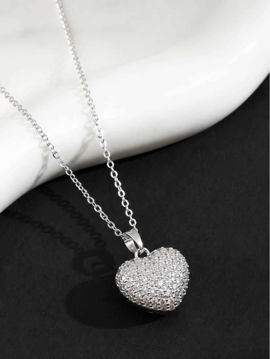 Puffy pavé heart pendant necklace on silver cable chain displayed against a dark background with marble prop