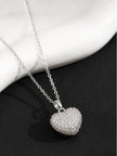 Puffy pavé heart pendant necklace on silver cable chain displayed against a dark background with marble prop