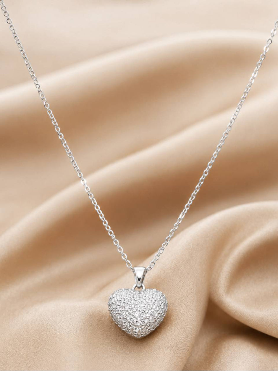 Silver CZ heart pendant necklace draped over soft beige satin fabric showing full chain length