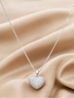Silver CZ heart pendant necklace draped over soft beige satin fabric showing full chain length