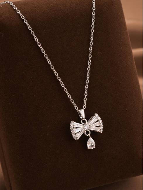 Silver bow pendant necklace with cubic zirconia stones displayed on a brown velvet jewellery tray