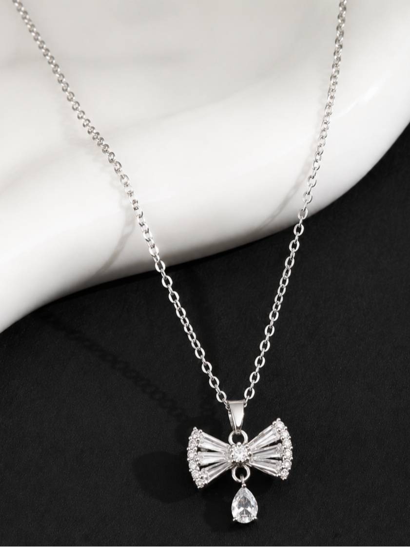 CZ bow necklace laid flat on a black and white marble surface showing full chain length