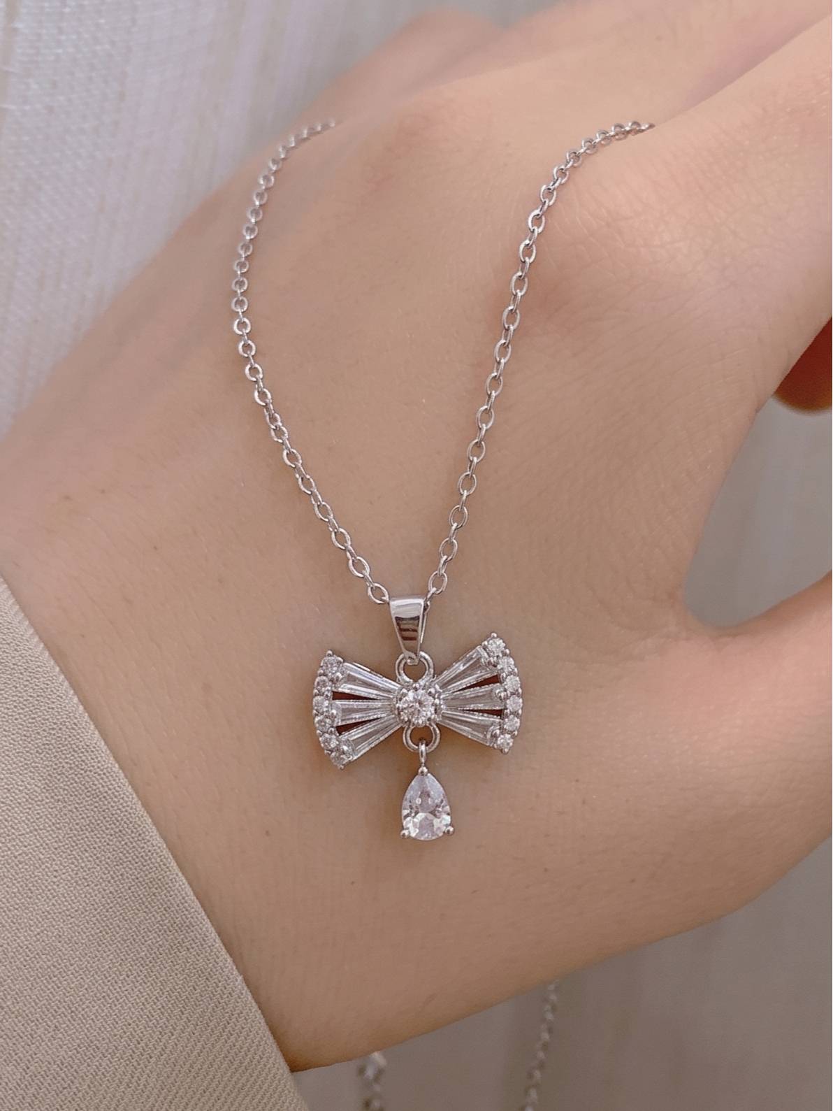 Close-up of silver bow pendant necklace draped over a model's hand showing stone detail