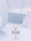 Silver cubic zirconia bow pendant necklace hanging against a soft blue background showing full silhouette