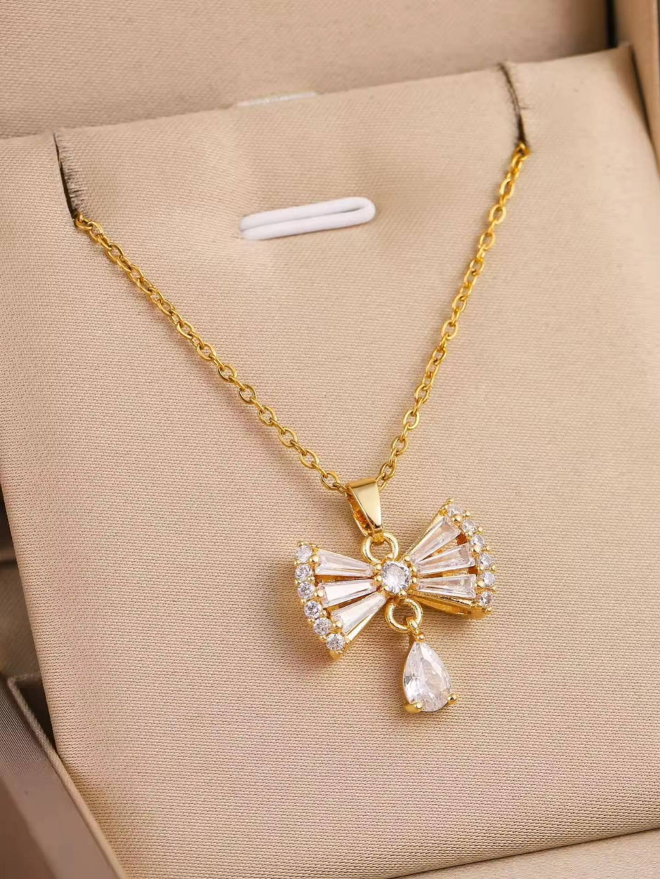 Gold-plated crystal bow pendant necklace displayed flat on a beige jewellery box