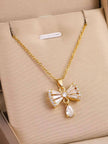 Gold-plated crystal bow pendant necklace displayed flat on a beige jewellery box