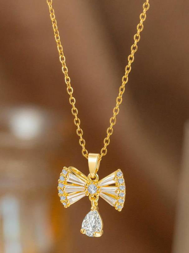 Crystal bow drop pendant necklace hanging against a warm brown blurred background