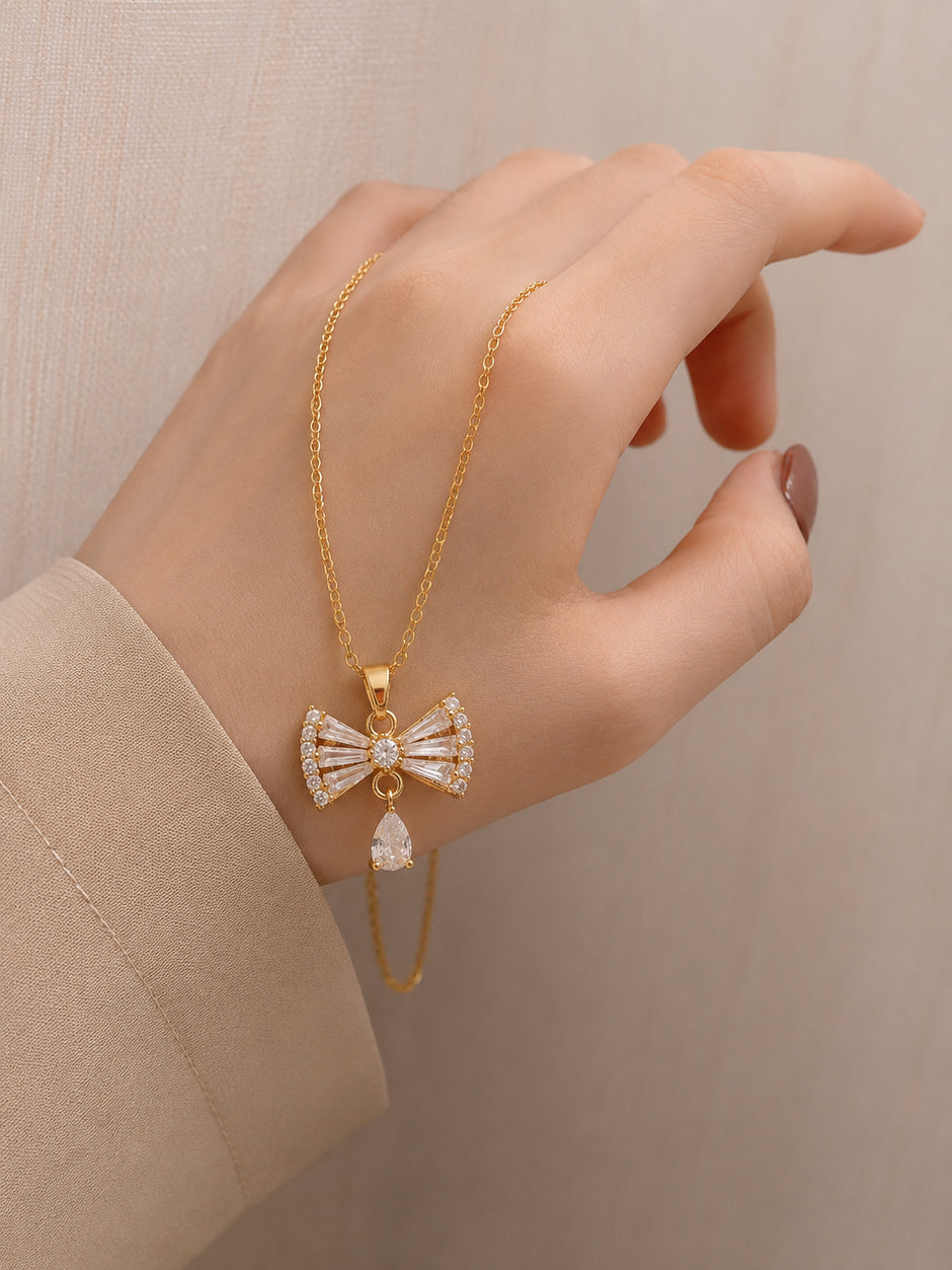 Model holding gold-plated bow pendant necklace between fingers wearing a beige blazer