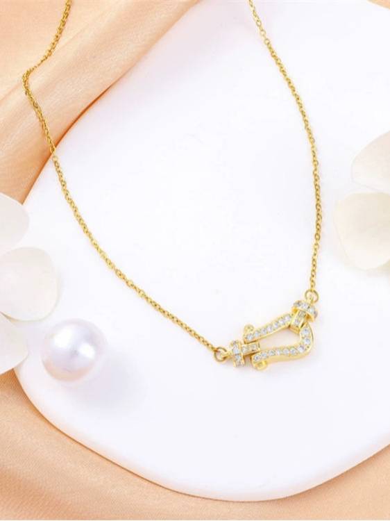 Gold-plated horseshoe CZ necklace laid flat on a white surface next to a pearl and white flower