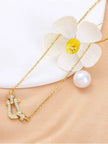 Close-up of horseshoe CZ pendant on gold cable chain beside a pearl and white daisy flower