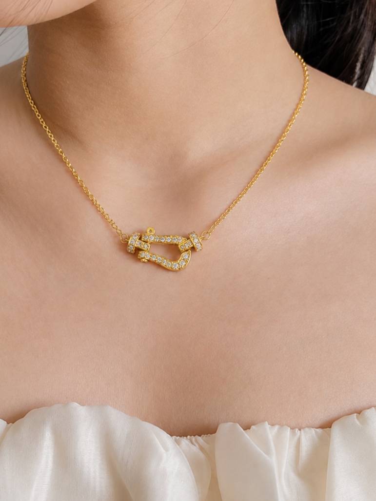 Woman wearing gold-plated CZ horseshoe necklace at collarbone over a white ruffled top