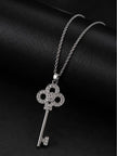 Close-up of pavé CZ quatrefoil key pendant lying flat on black leather surface with chain