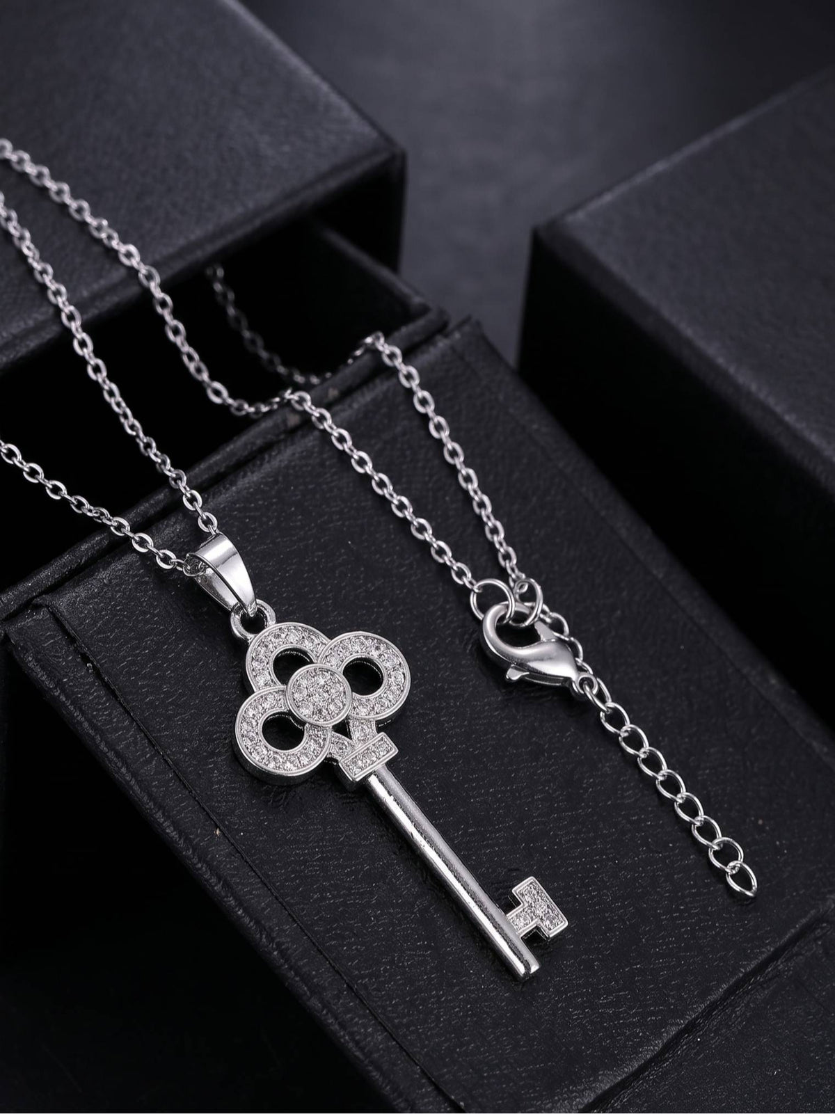 Key pendant necklace with lobster clasp and extender chain laid out on black jewellery boxes