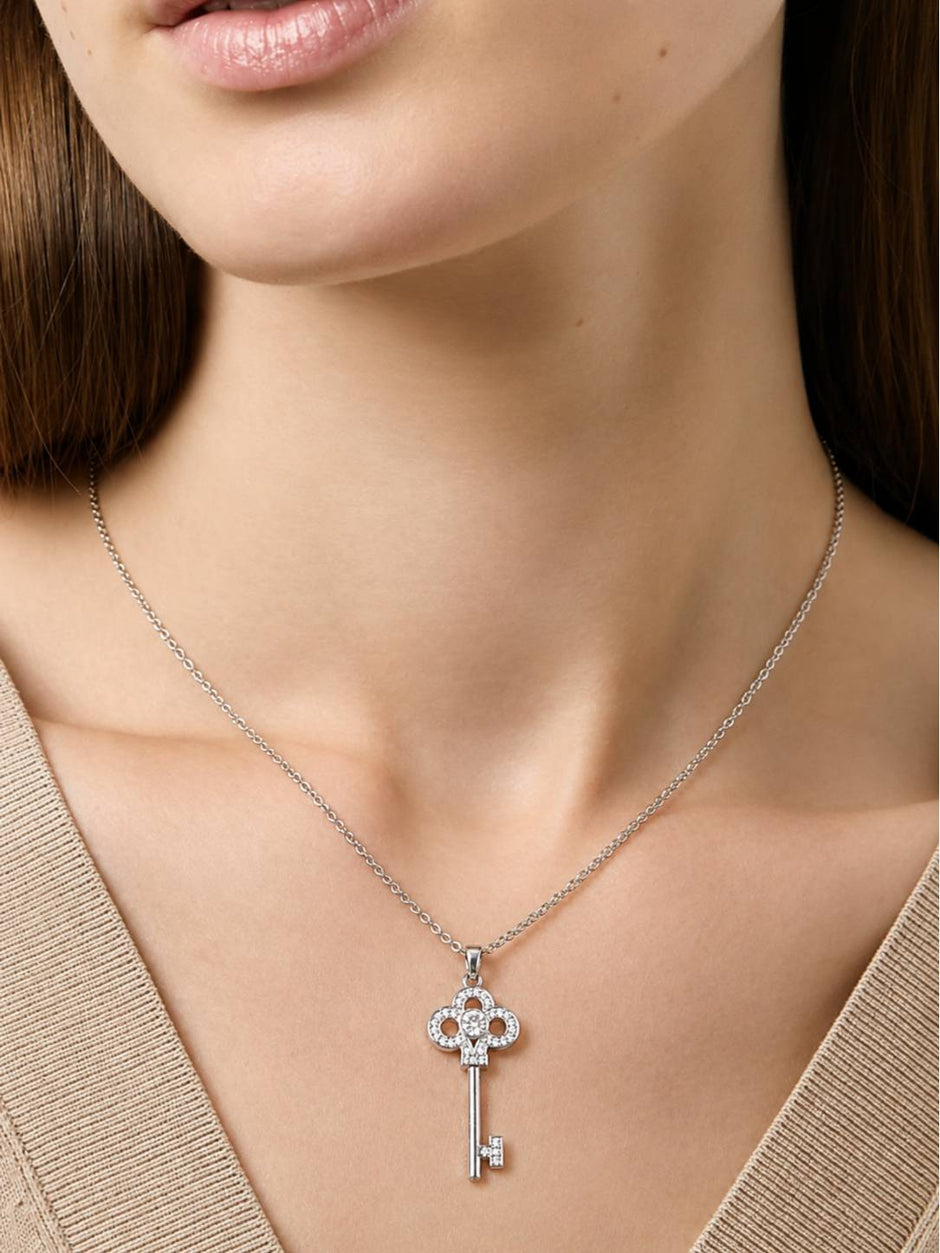 Woman wearing silver cubic zirconia key pendant necklace over a beige V-neck top, collarbone view