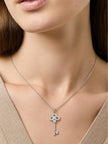 Woman wearing silver cubic zirconia key pendant necklace over a beige V-neck top, collarbone view