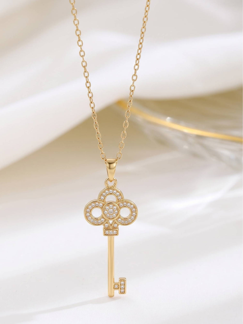 Close-up of gold-plated trefoil key pendant with CZ setting on white fabric
