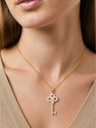 Woman wearing gold-plated key pendant necklace over a beige ribbed V-neck top