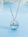 Silver-tone circular pendant necklace with aqua crystal and whale charm on blue background