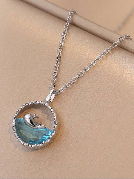 Side view of whale ocean pendant necklace showing faceted blue crystal on beige surface
