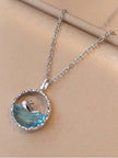 Side view of whale ocean pendant necklace showing faceted blue crystal on beige surface