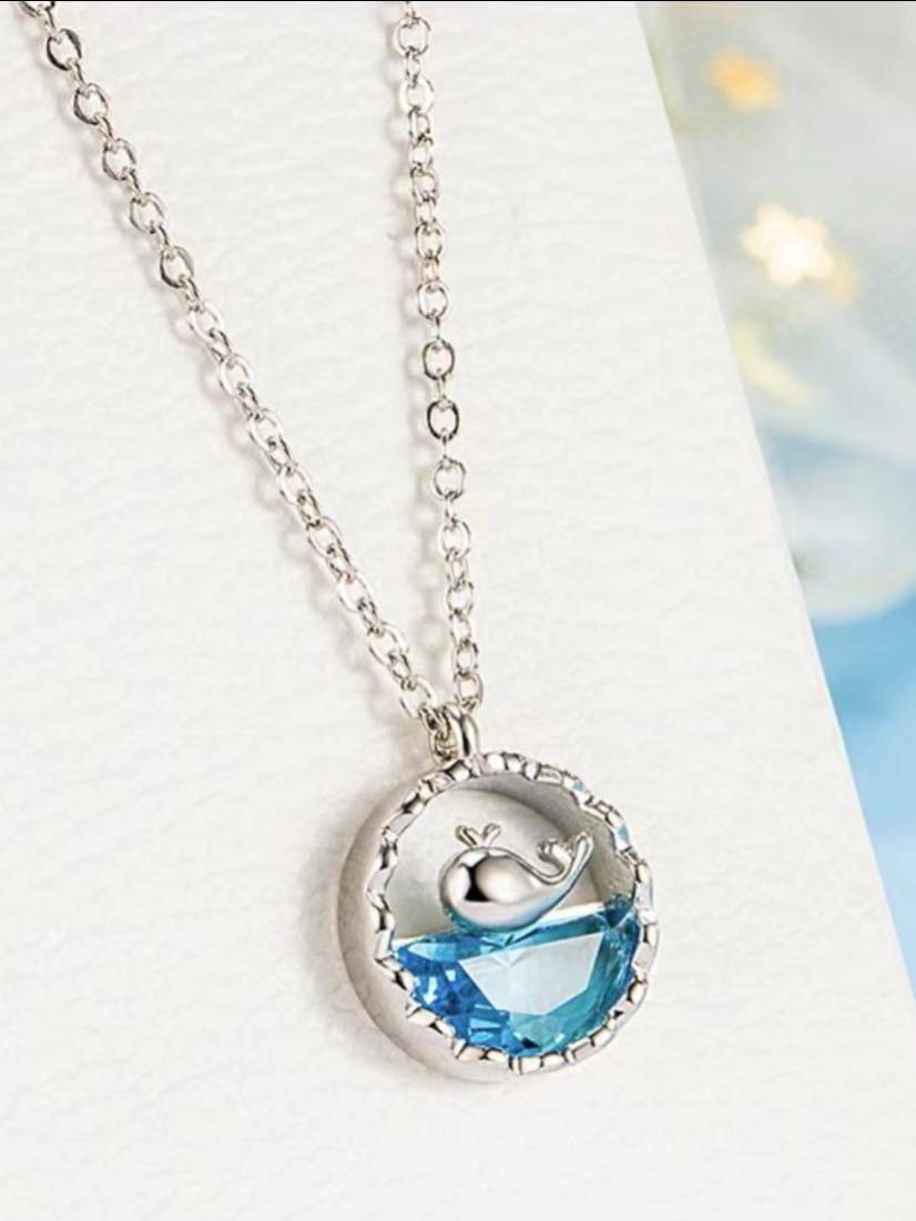 Close-up of silver whale charm sitting above blue crystal in textured circular pendant frame