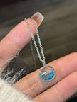 Hand holding small silver whale ocean pendant necklace to show actual size scale