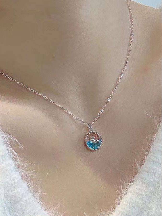 Whale ocean crystal pendant necklace worn around a woman's neck over a white fuzzy top