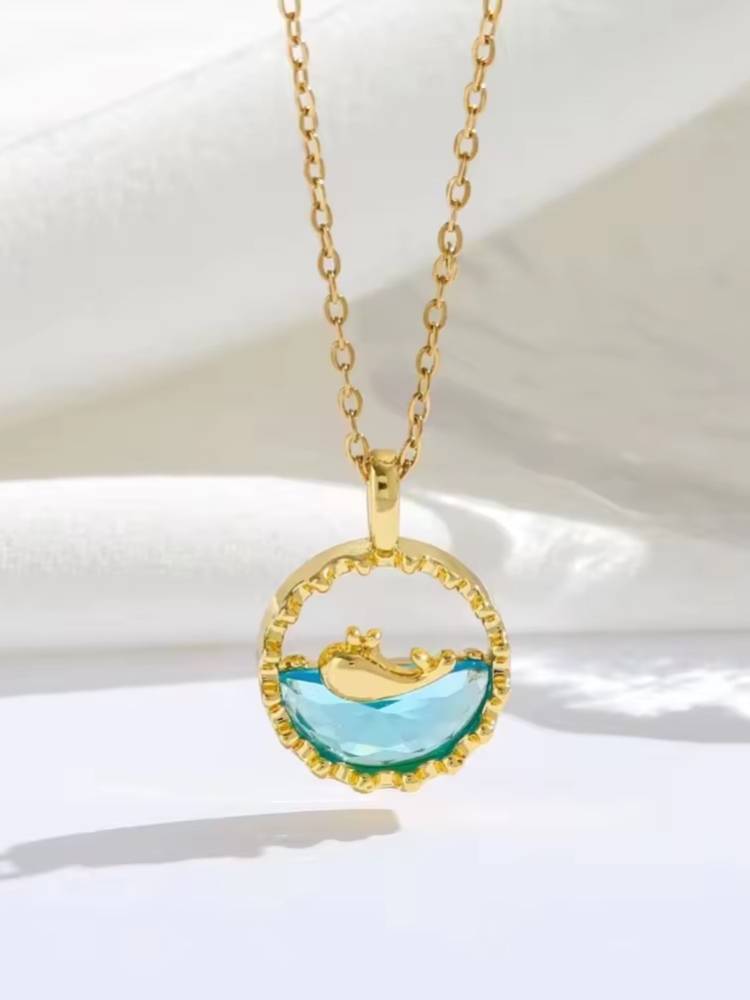 Gold-plated circular pendant with aqua crystal and dolphin detail hanging on cable chain against white fabric