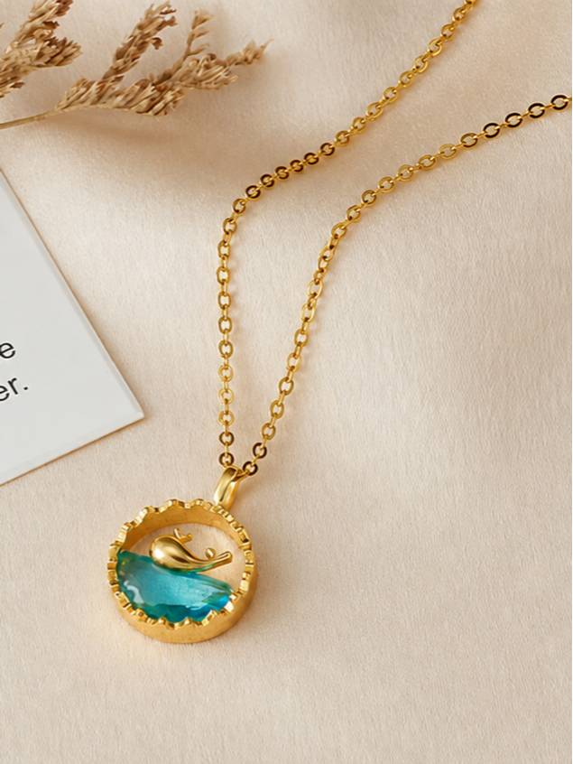 Gold wave crystal pendant necklace resting on beige surface beside dried flowers and handwritten note card