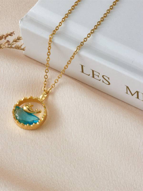Close-up of aqua blue crystal dolphin pendant necklace propped against spine of white hardcover book
