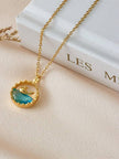 Close-up of aqua blue crystal dolphin pendant necklace propped against spine of white hardcover book