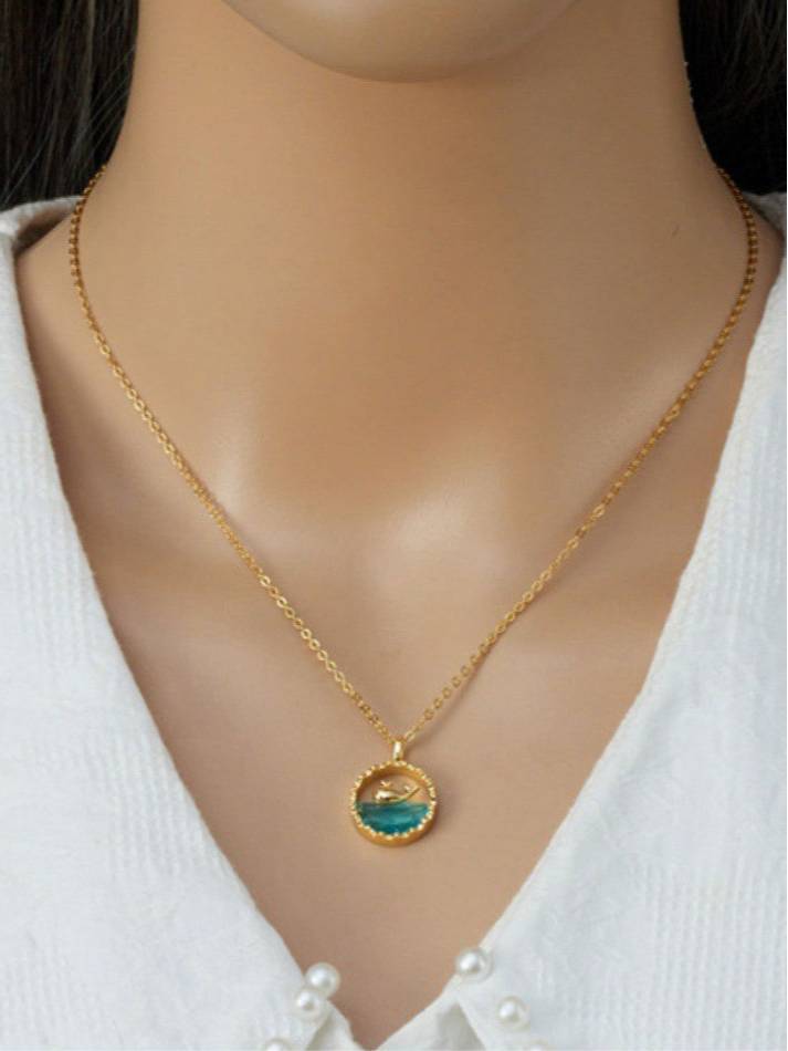 Model wearing gold ocean wave crystal pendant necklace at collarbone over white knit sweater