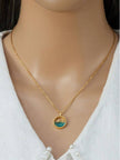 Model wearing gold ocean wave crystal pendant necklace at collarbone over white knit sweater