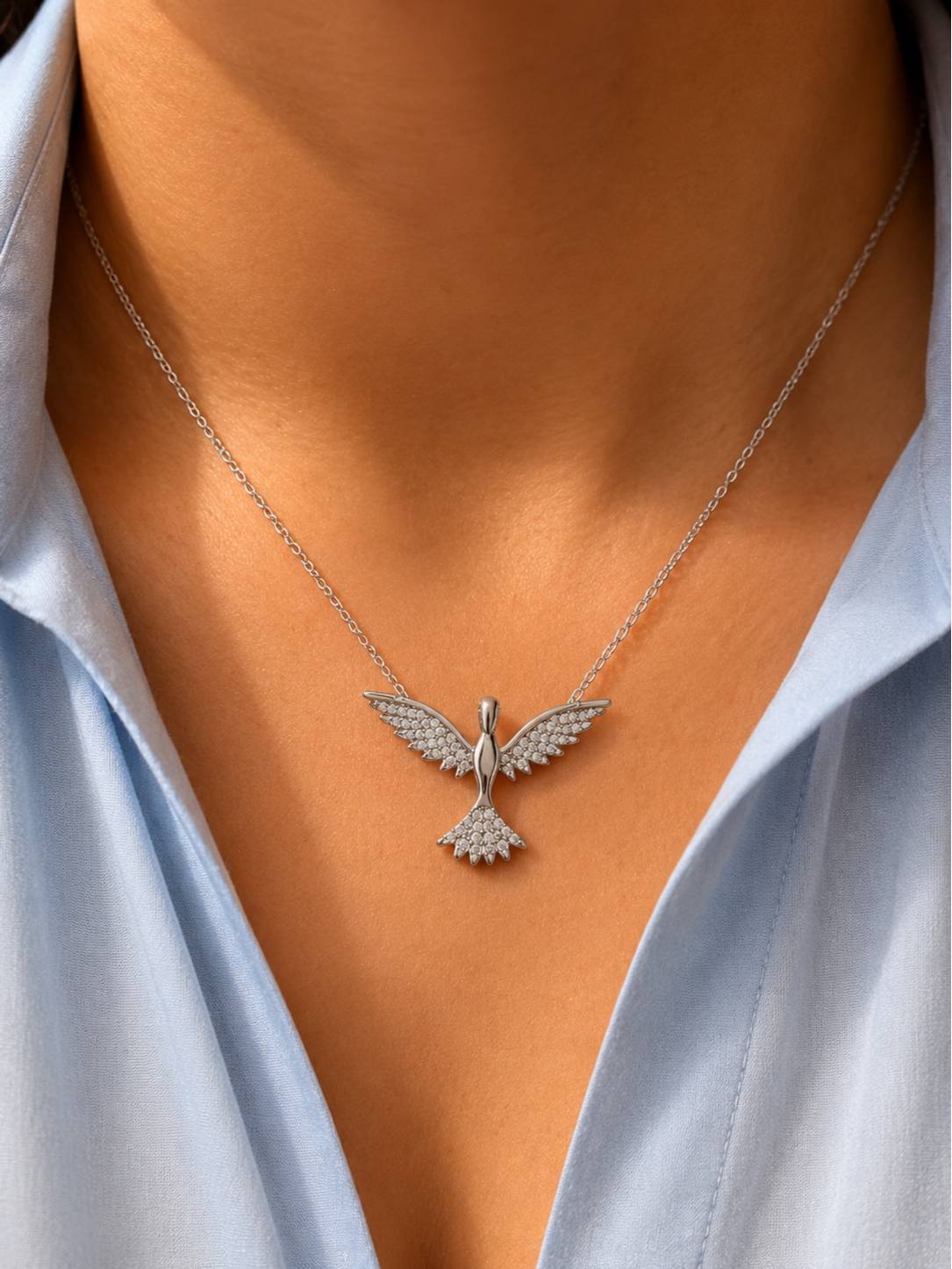 Silver CZ bird pendant necklace worn on a woman in a light blue shirt