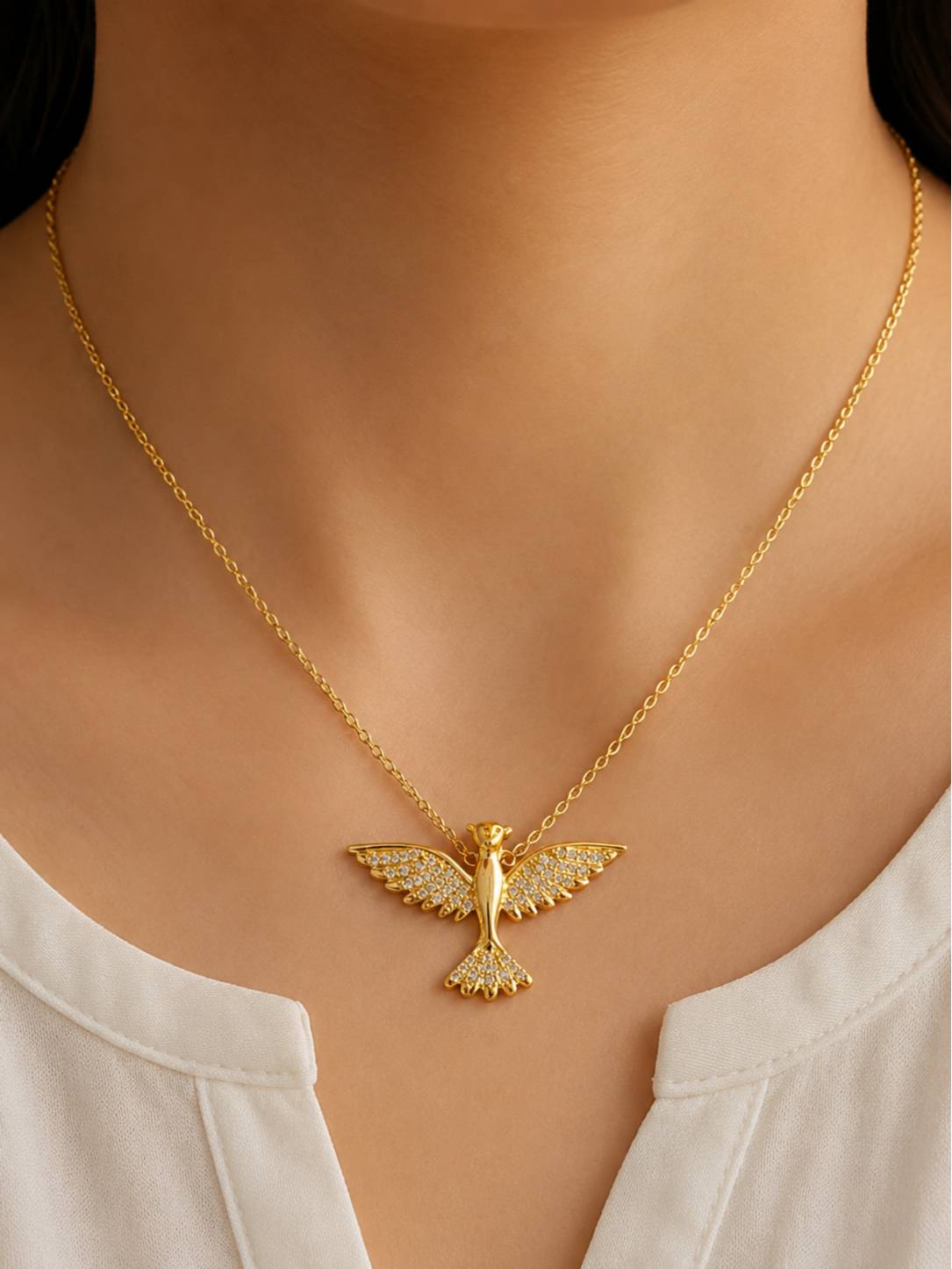 Woman wearing gold crystal bird pendant necklace over a white top showing fit at neckline