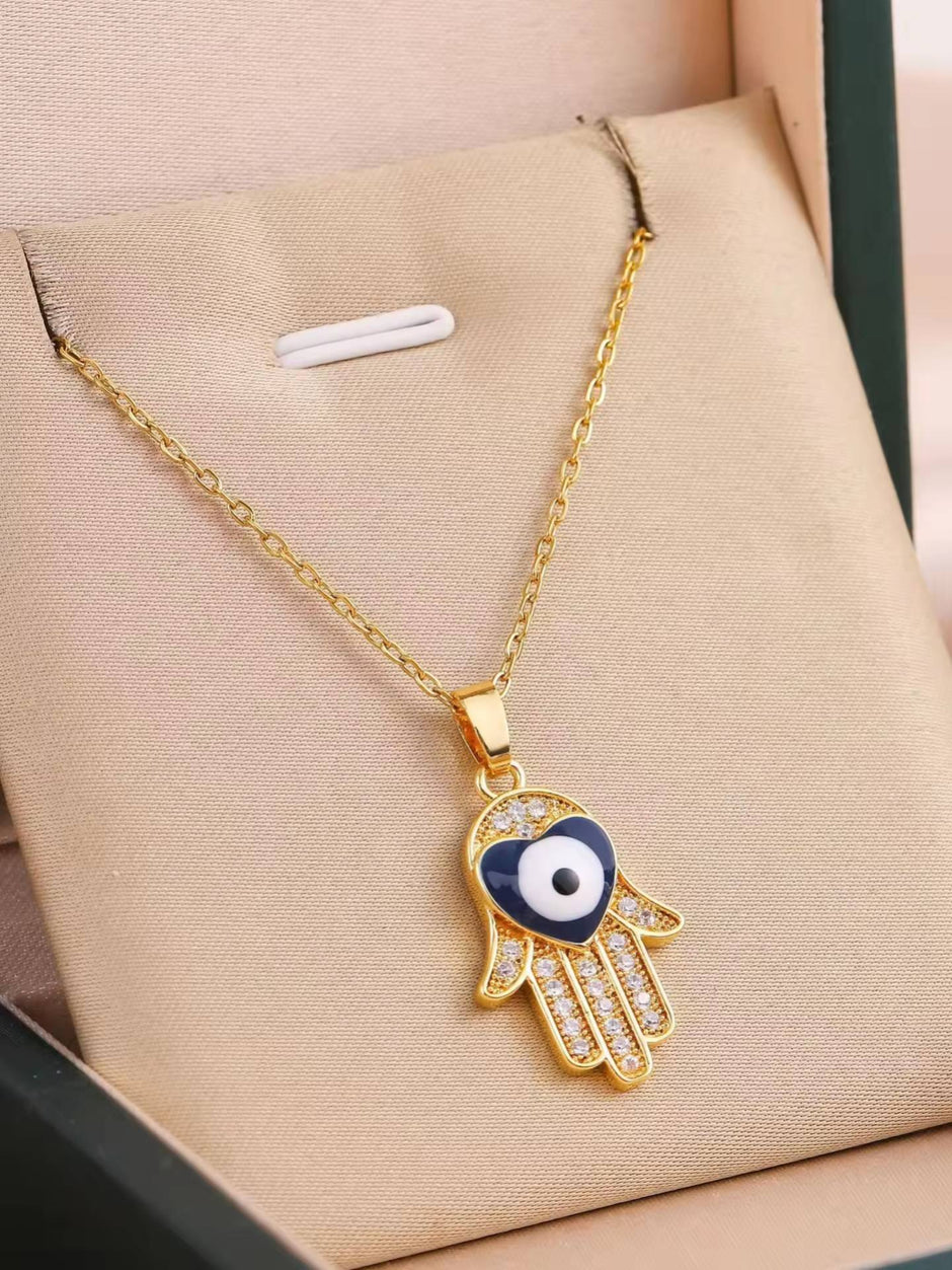 Gold-plated Hamsa hand evil eye pendant necklace displayed inside a green jewellery box on beige fabric
