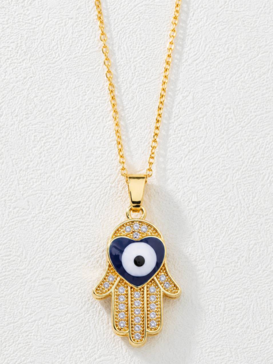 Close-up of Hamsa hand pendant with navy blue heart-shaped evil eye and cubic zirconia stones on white background