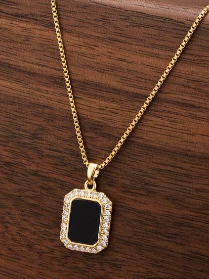 Gold-plated rectangular black pendant necklace with CZ halo resting on dark wooden surface