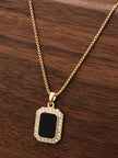 Gold-plated rectangular black pendant necklace with CZ halo resting on dark wooden surface