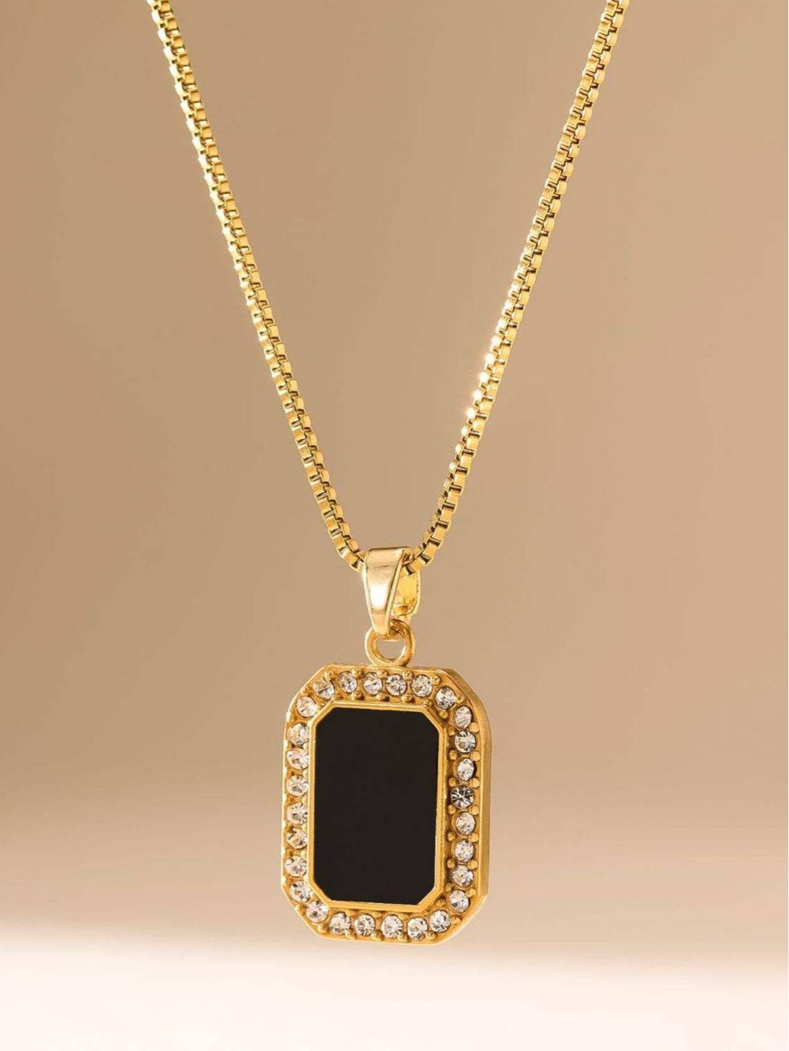 Full view of gold box chain necklace with black enamel and cubic zirconia pendant on beige background