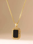 Full view of gold box chain necklace with black enamel and cubic zirconia pendant on beige background